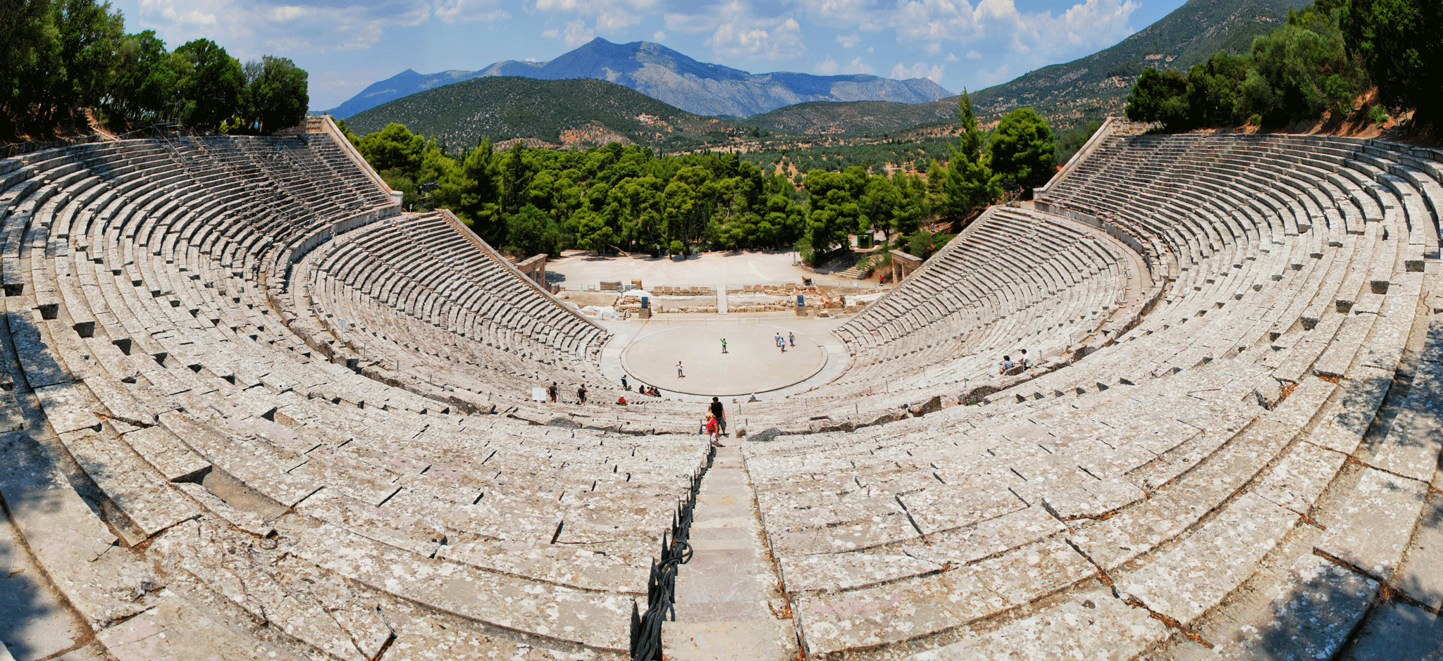 Panoramic view of the Ancient Theatre of Epidaurus, Greece, showcasing its vast, well-preserved stone seating and the scenic landscape beyond.