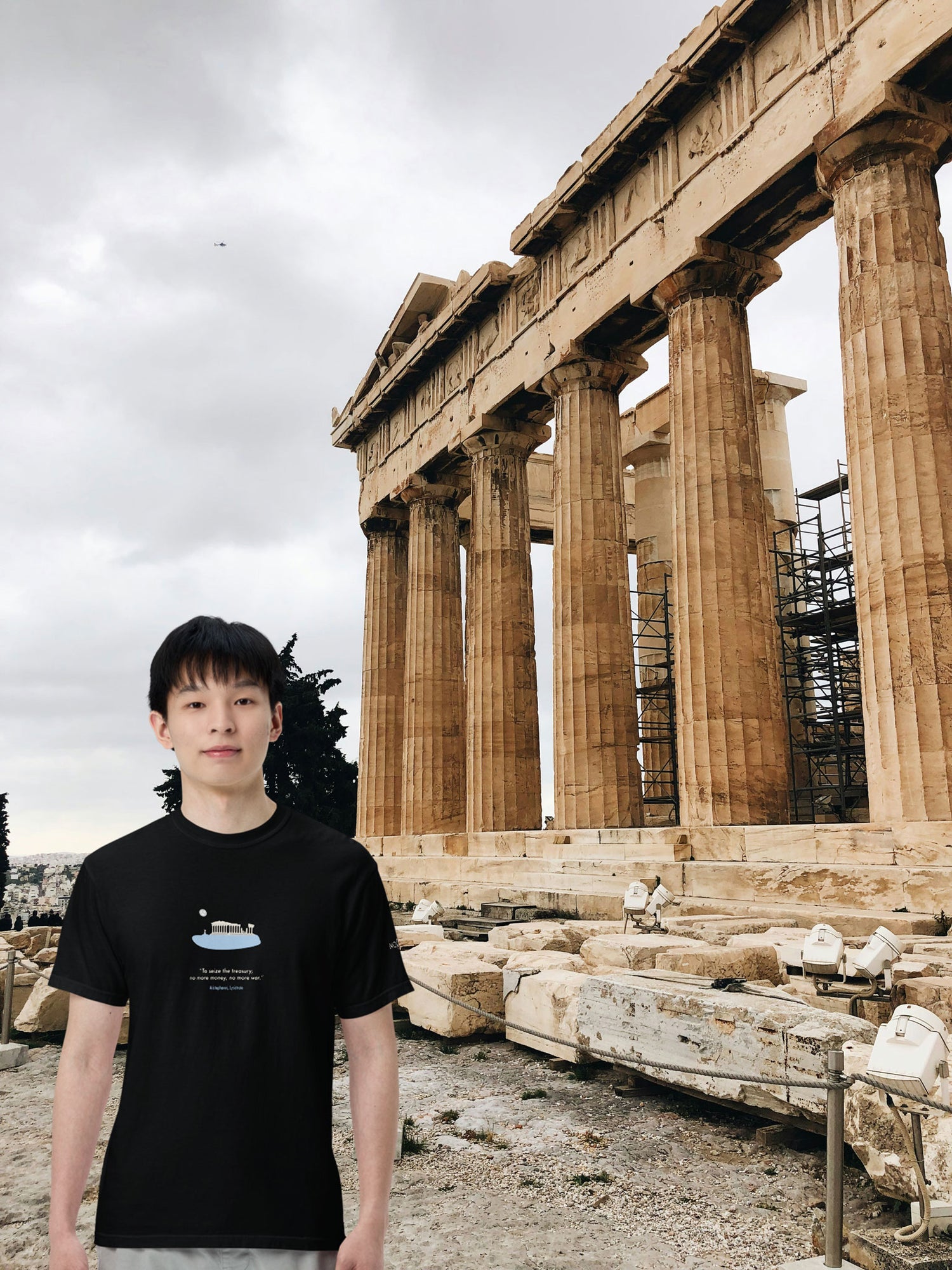 Young man wearing a black unisex NOMADkit T-shirt with Acropolis Parthenon graphic, posing in front of the Parthenon, Athens.