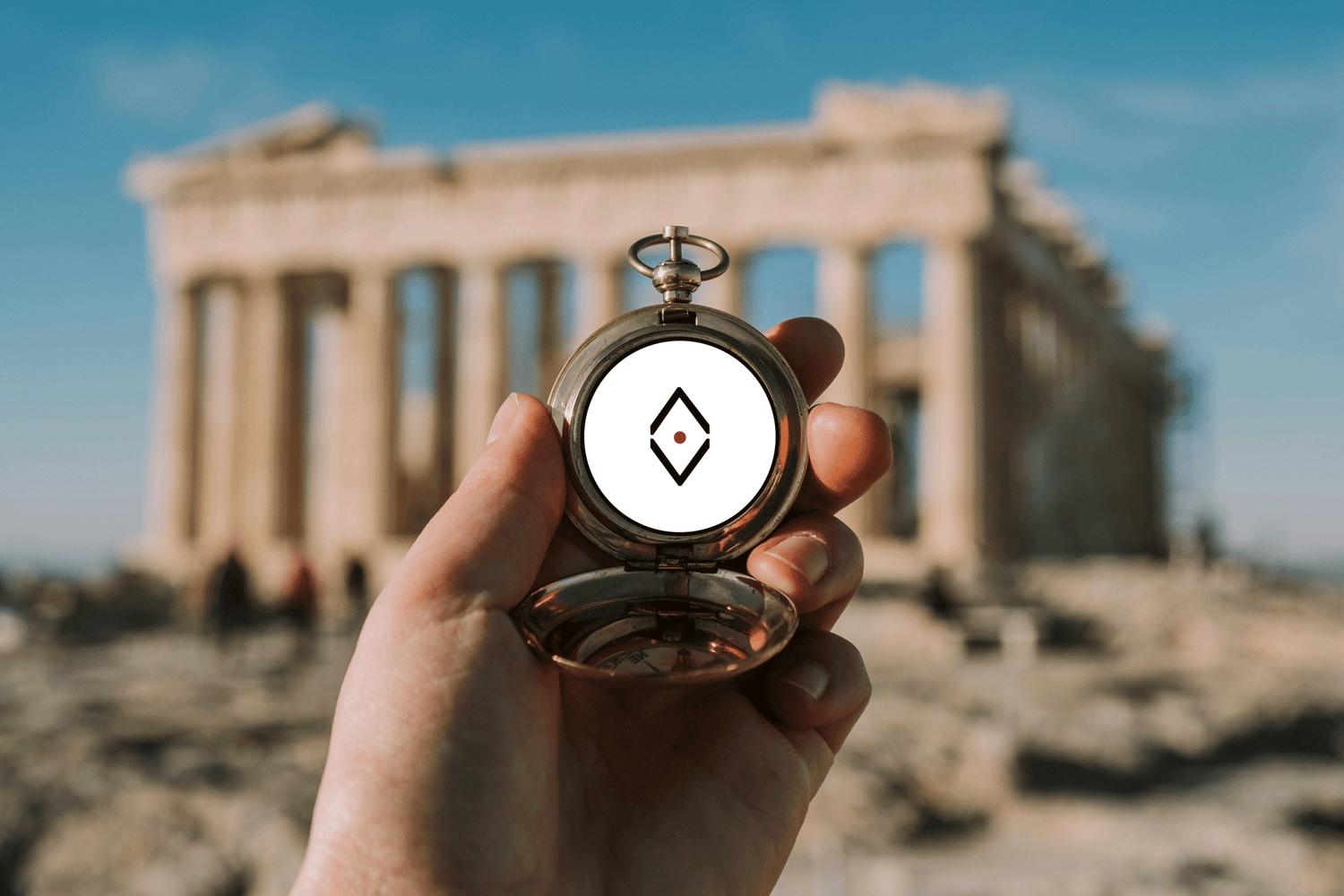 A GIRL'S hand holding a vintage NOMADkit sign compass with the iconic Parthenon of Athens in the background, symbolizing NOMADkit’s commitment to guiding travelers through authentic and culturally rich journeys.