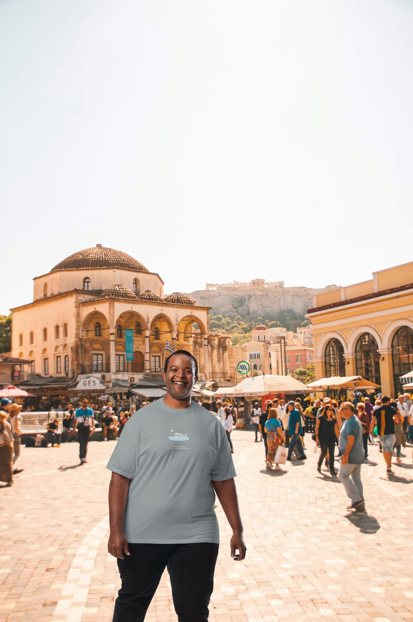 Man wearing an ice blue unisex NOMADkit T-shirt with Parthenon Athens design, standing in Monastiraki Square, Athens.