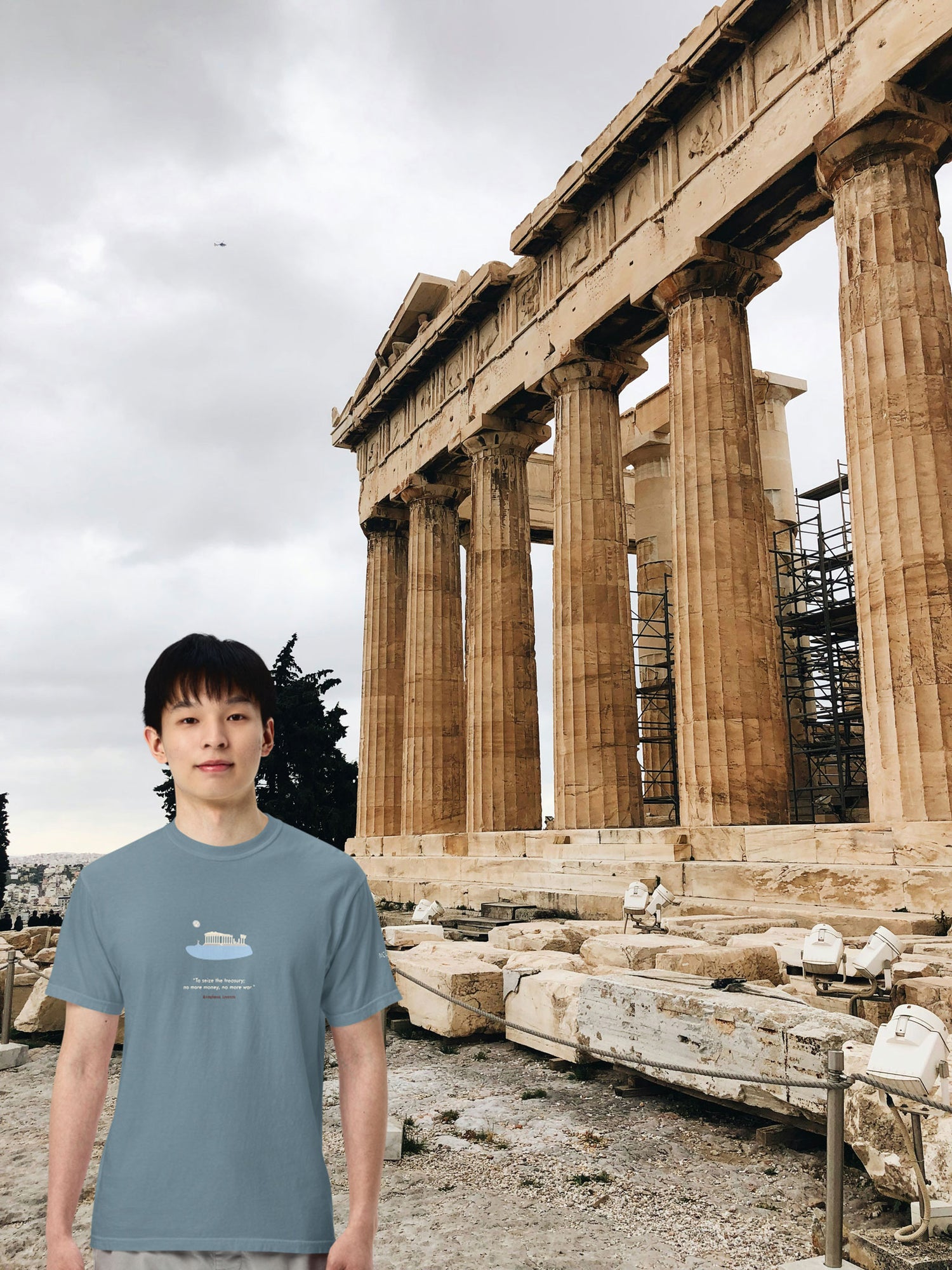 Young man in an ice blue unisex NOMADkit T-shirt with Parthenon Athens print, posing in front of the Parthenon, Athens.